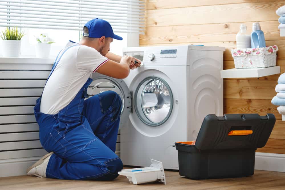 A technician repairing a washing machine in a laundry room
